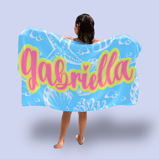 Person wearing a blue towel with 'Gabriella' printed on it against a light gray background