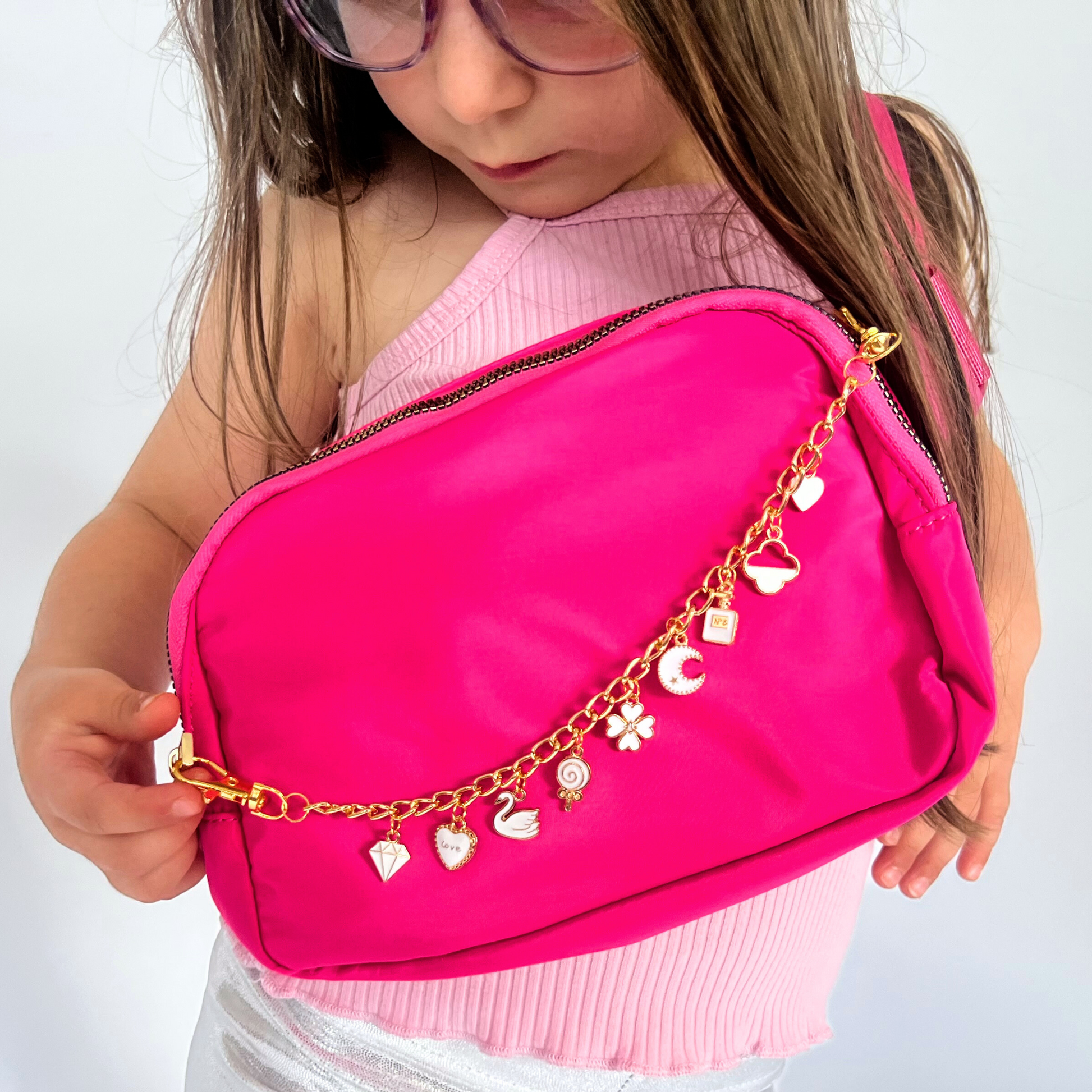 Child holding a pink bag with gold chain and charms on a white background