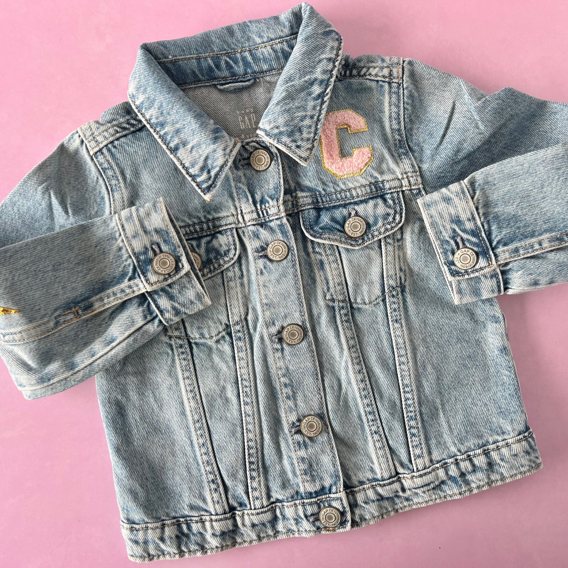 Denim jacket with a pink letter 'C' patch on a pink background