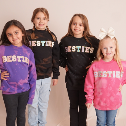 Four children wearing 'BESTIES' sweatshirts in various colors on a plain background