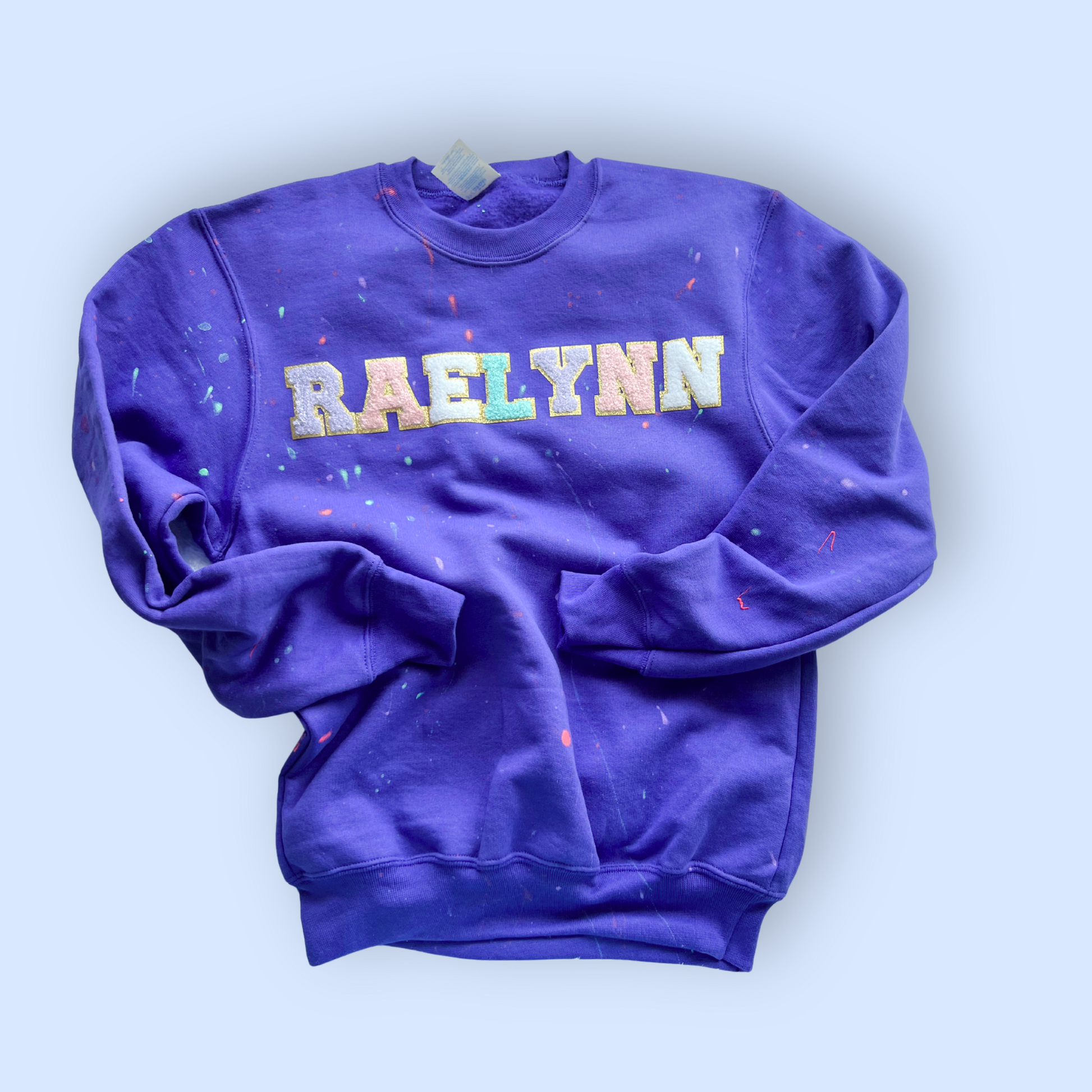 Purple sweatshirt with 'RAELYNN' printed on it against a light blue background
