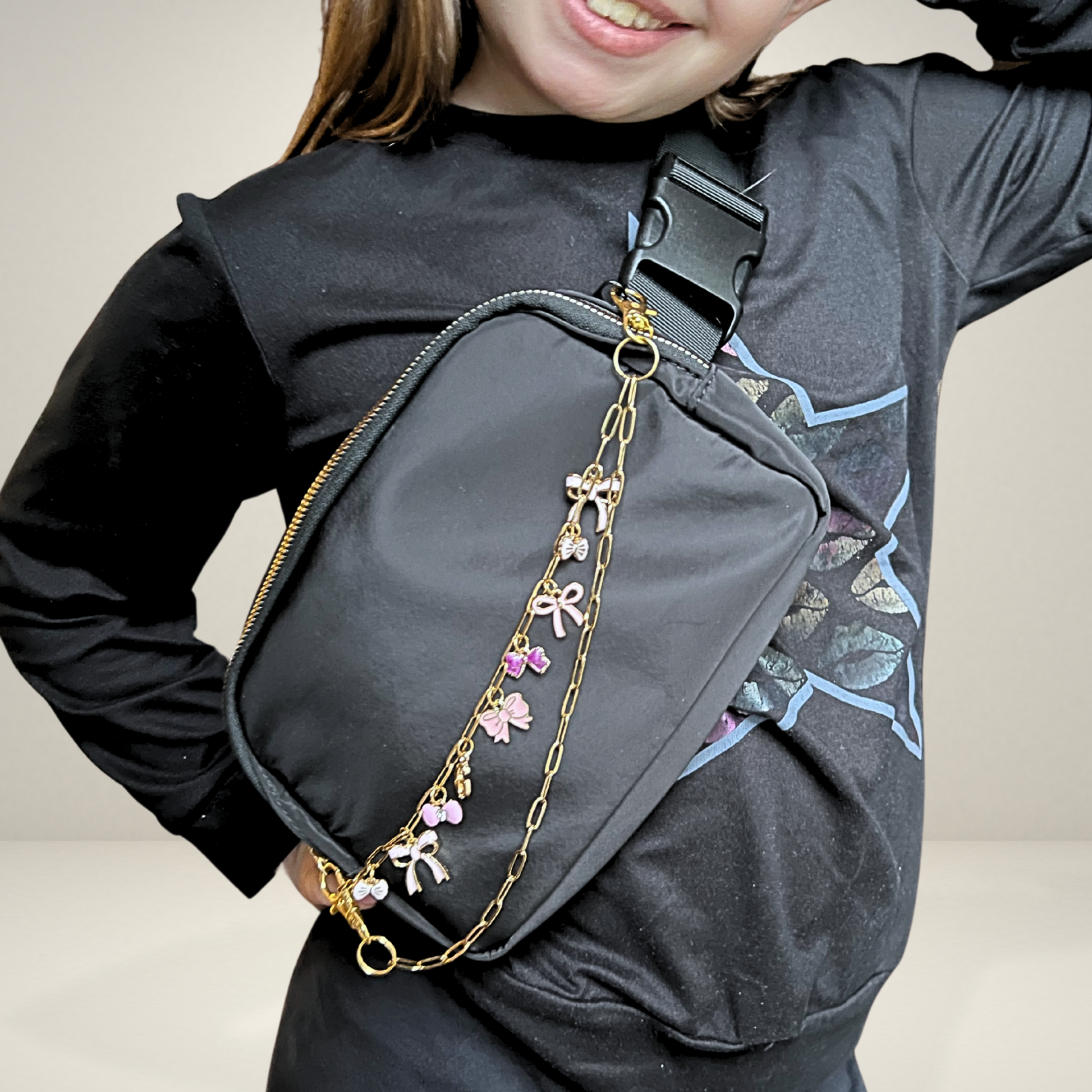 Person wearing a black crossbody bag with decorative chains and charms on a plain background