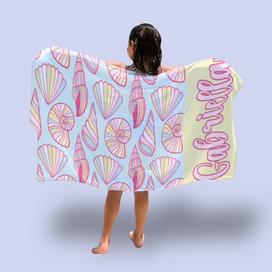 Person holding a colorful towel with shell pattern and 'Gabriella' text on a light blue background