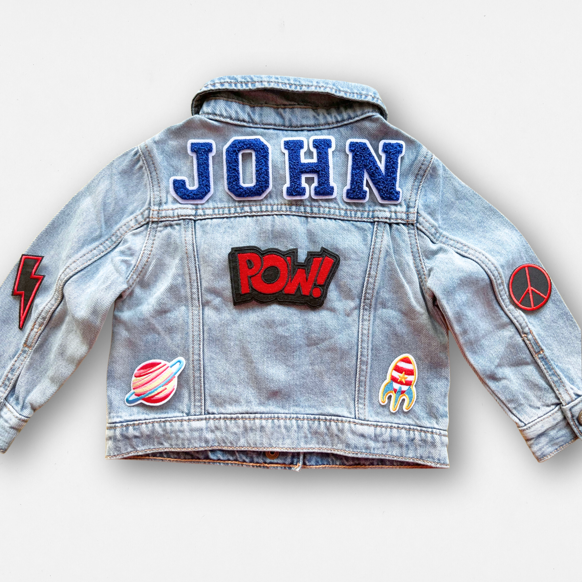 Denim jacket with patches including 'JOHN', 'POW!', and various other designs on a white background.