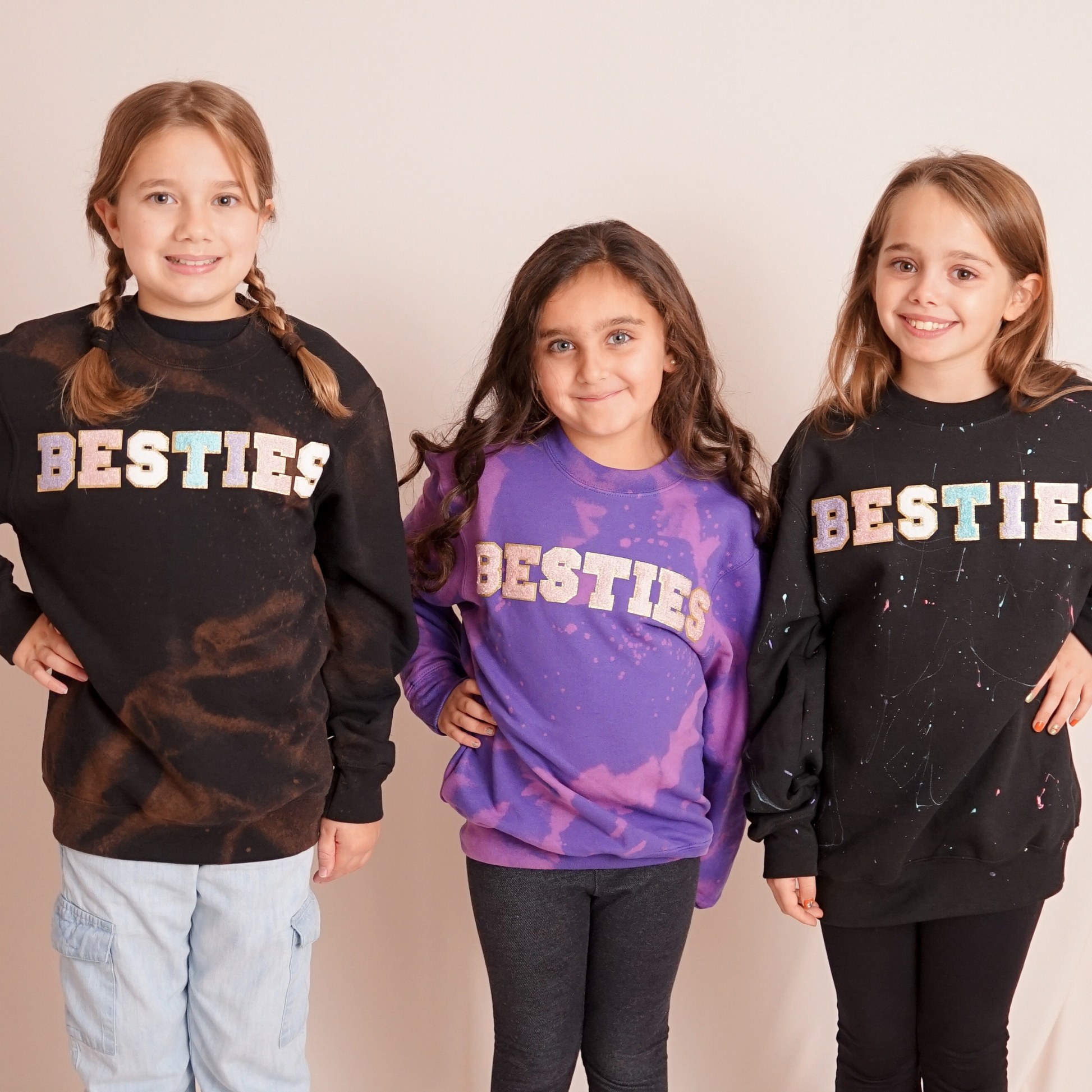 Three children wearing 'BESTIES' sweatshirts on a plain background