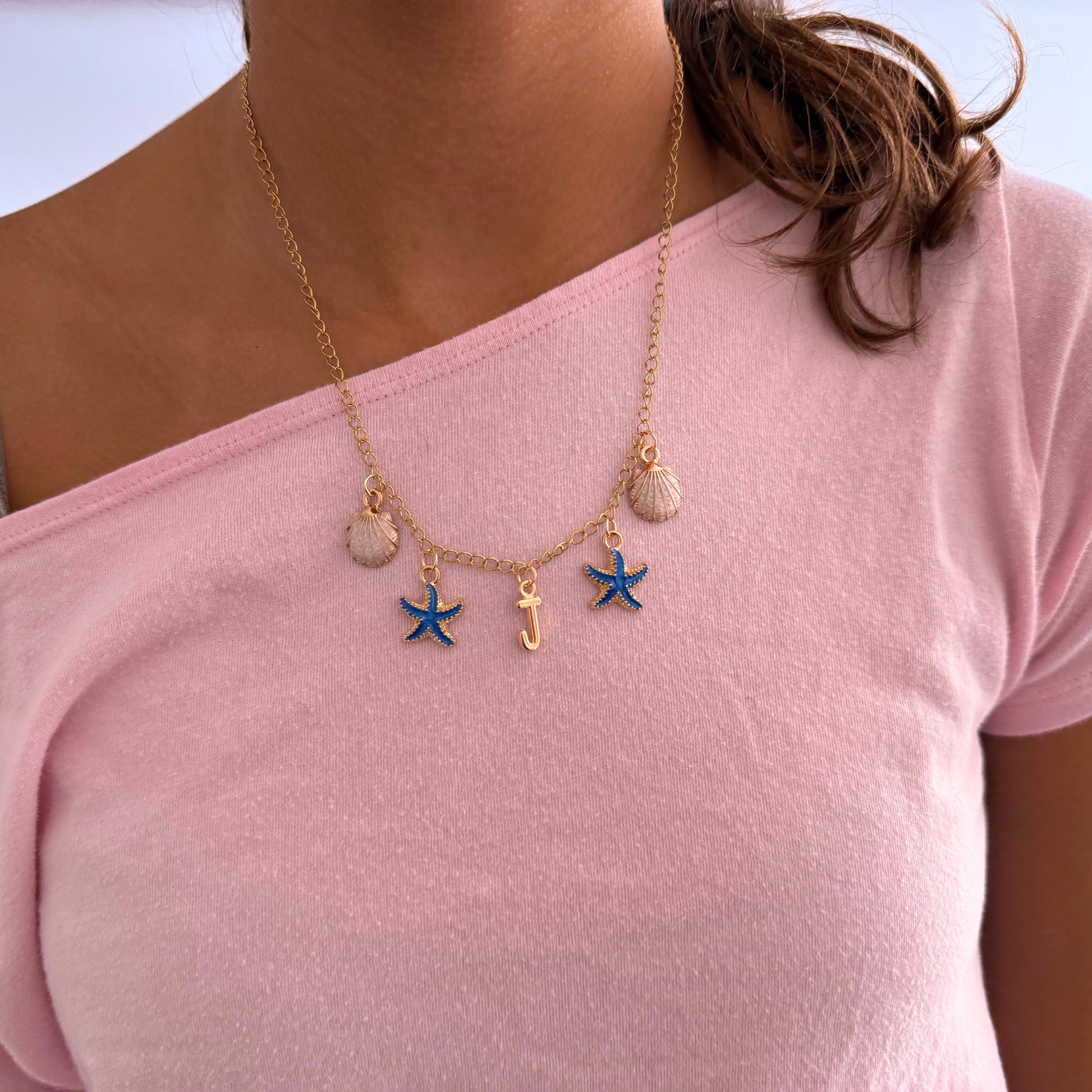 Necklace with starfish and shell charms worn by a person on a pink shirt