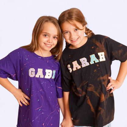 two girls wearing t shirts with their names across the chest. the names are spelled in colorful chenille letter patches