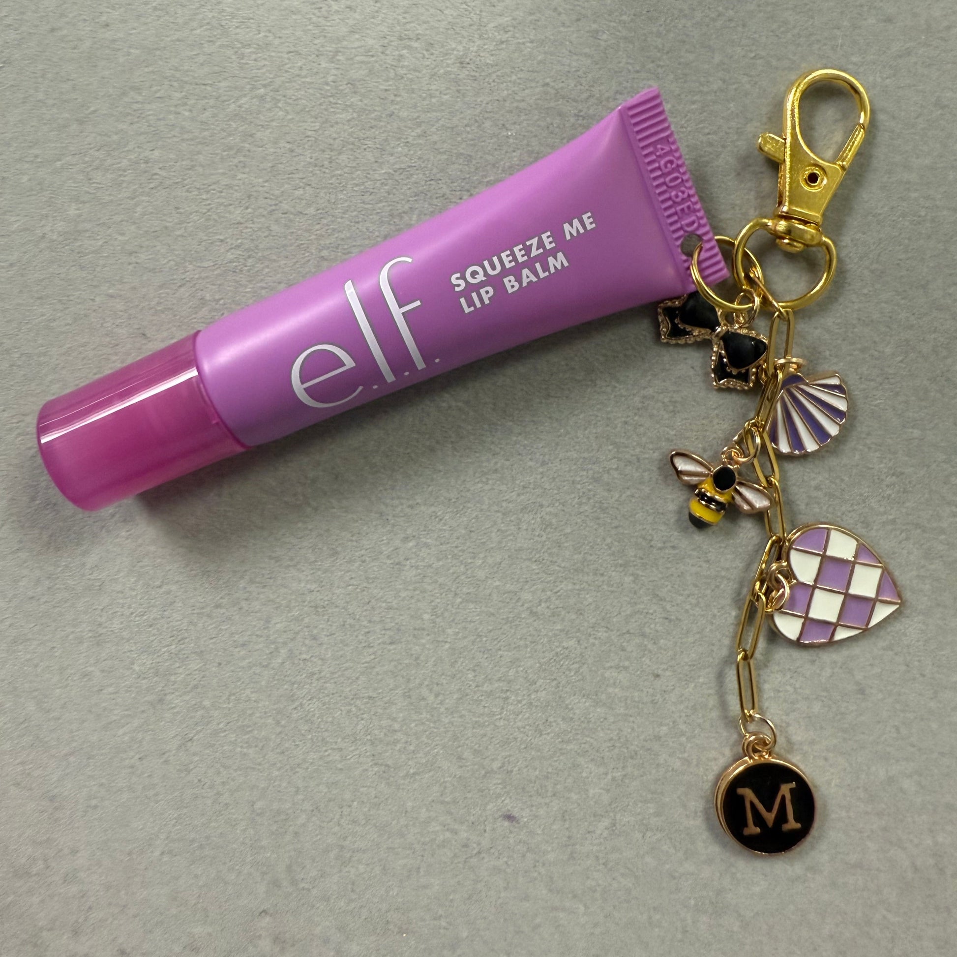 Purple lip balm keychain with charms on a gray background