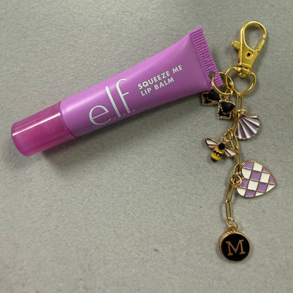 Purple lip balm keychain with charms on a gray background