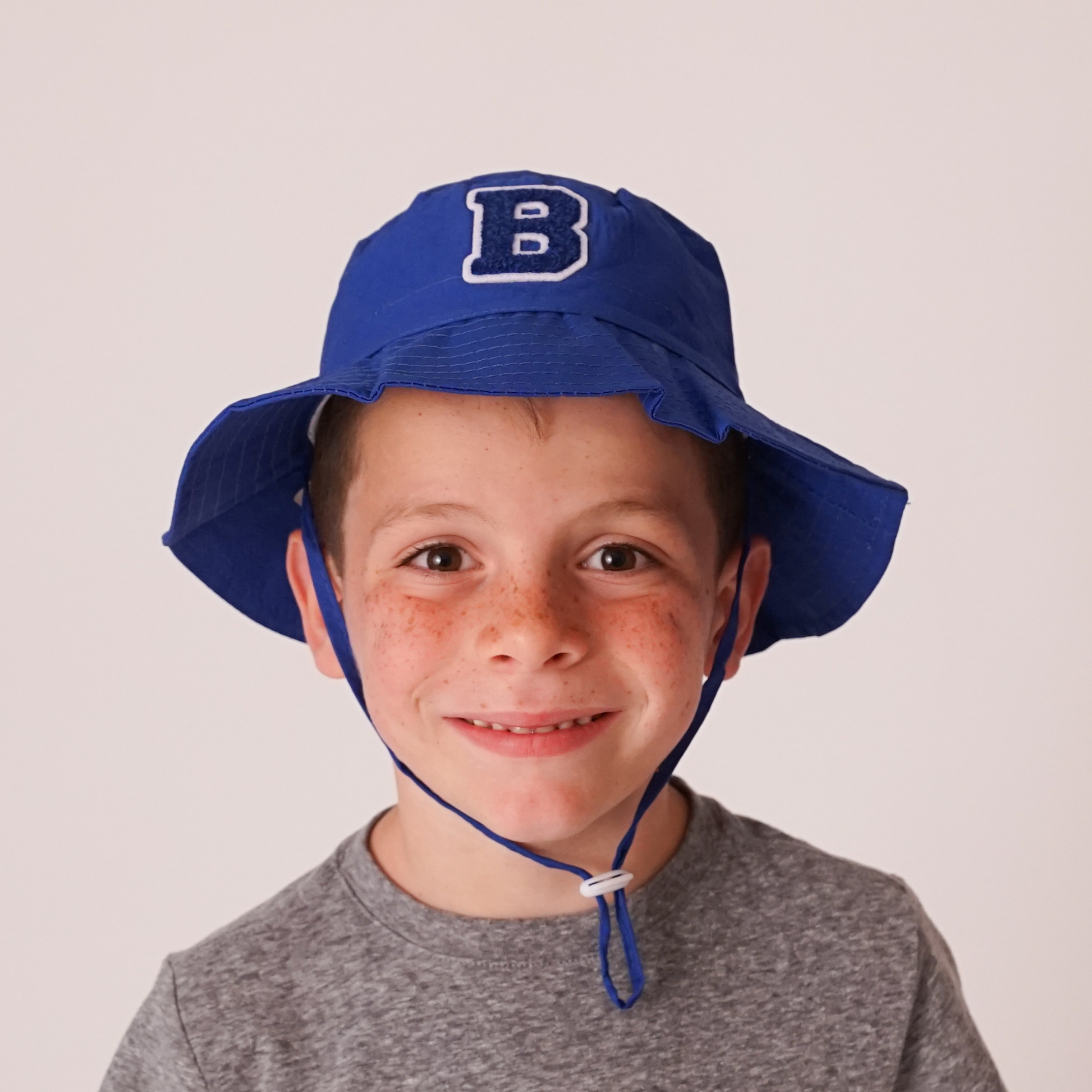 young boy wearing blue personalized sun hat with initial patch outdoors