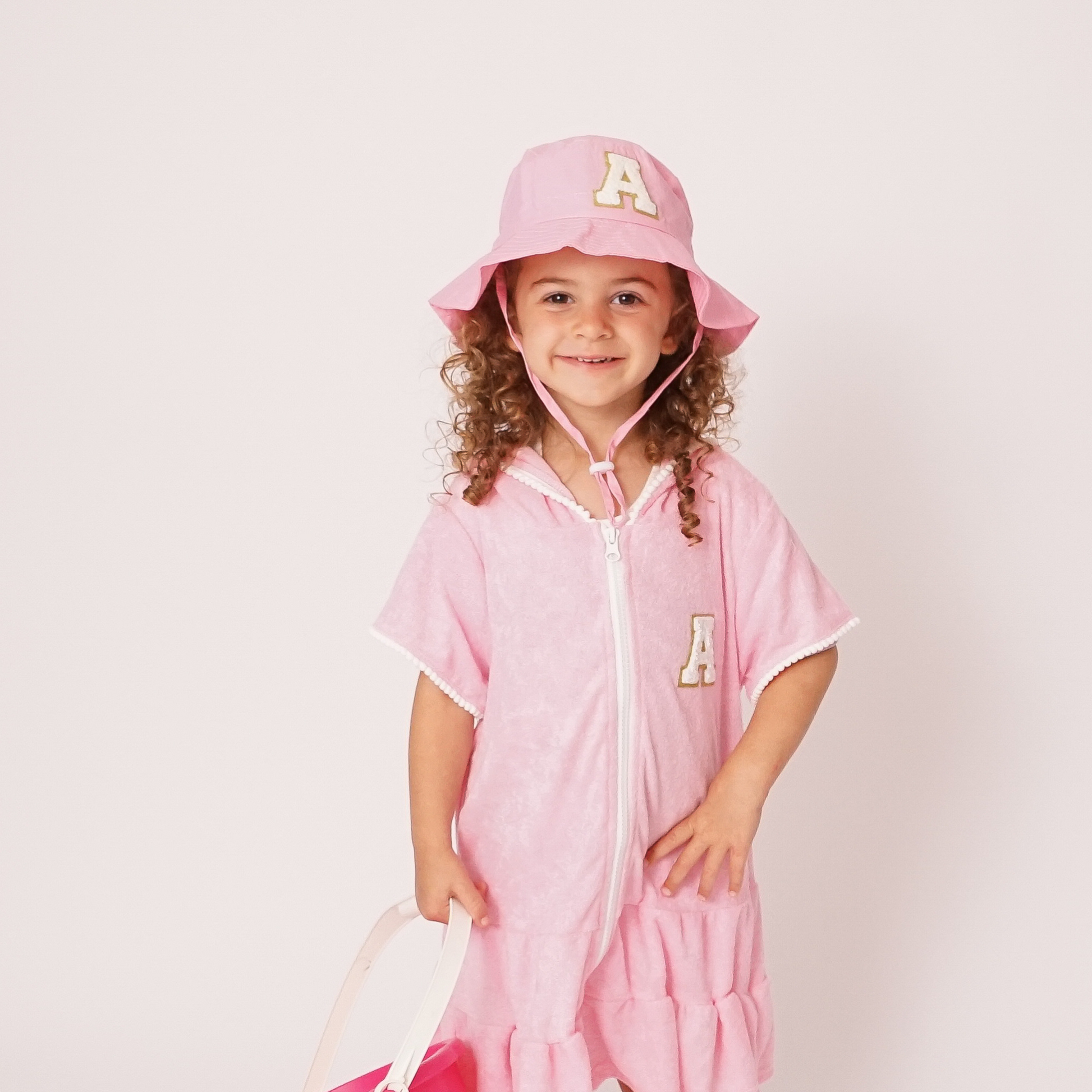 Pink toddler bucket hat with monogram patch styled on flat surface