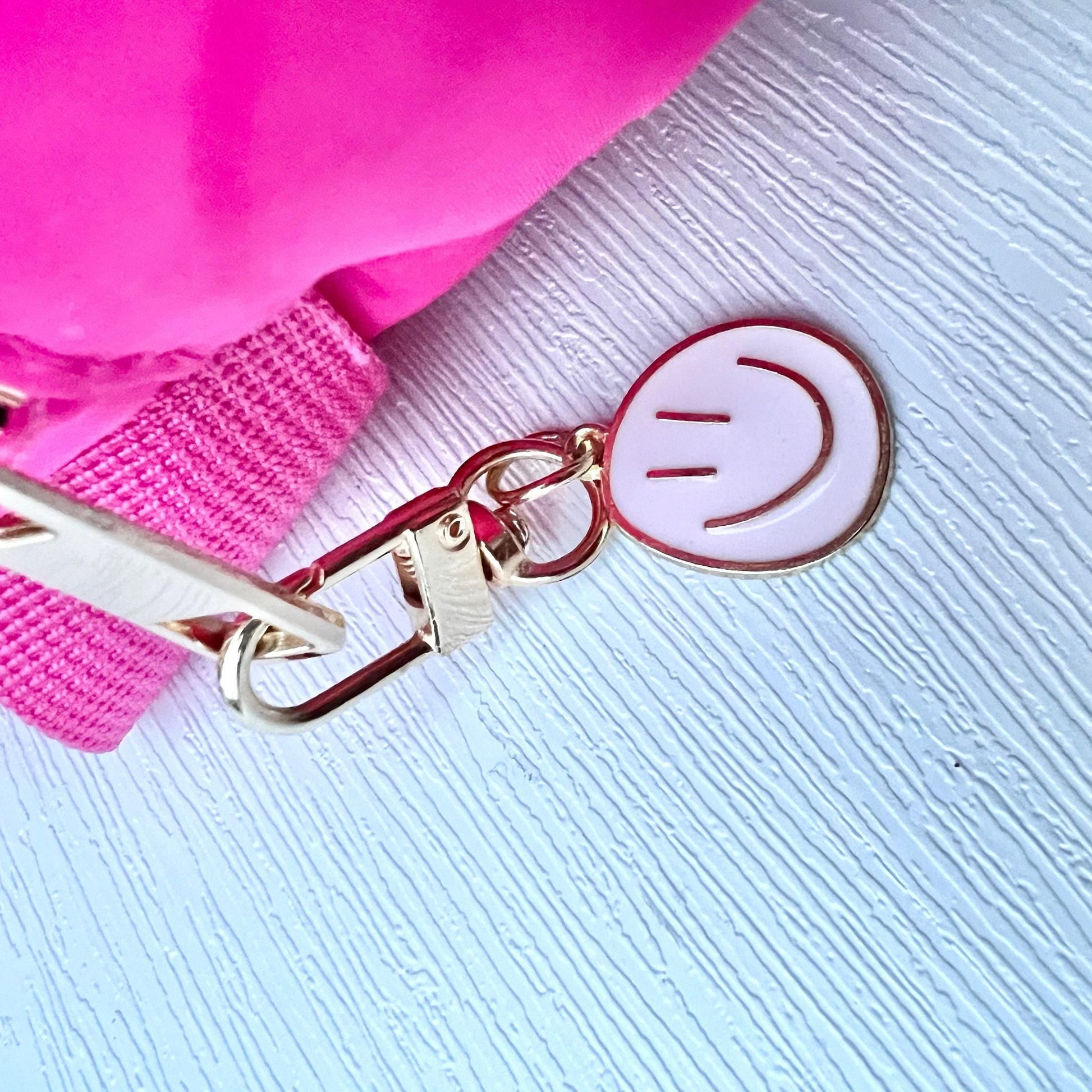 Pink bag with a smiley face keychain on a light blue textured background