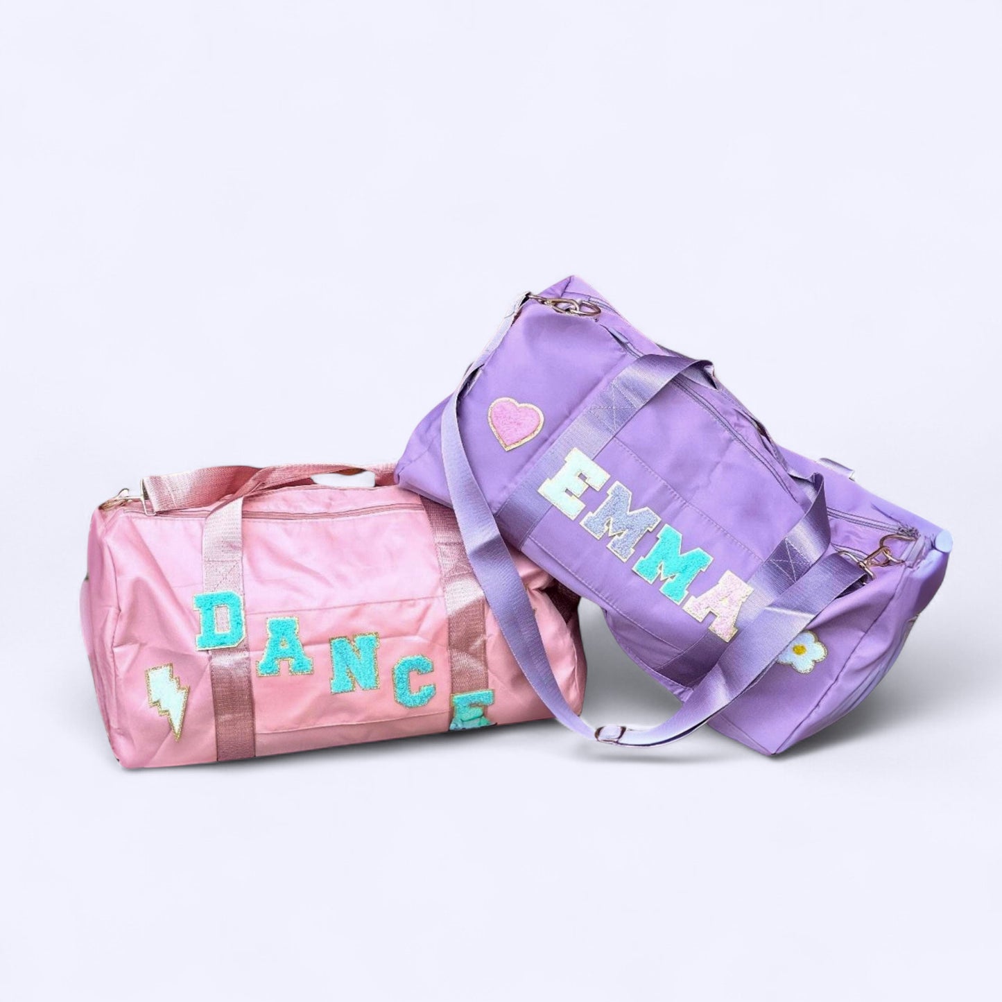 Two custom duffle bags with chenille patches spelling DANCE and EMMA in pink and purple.