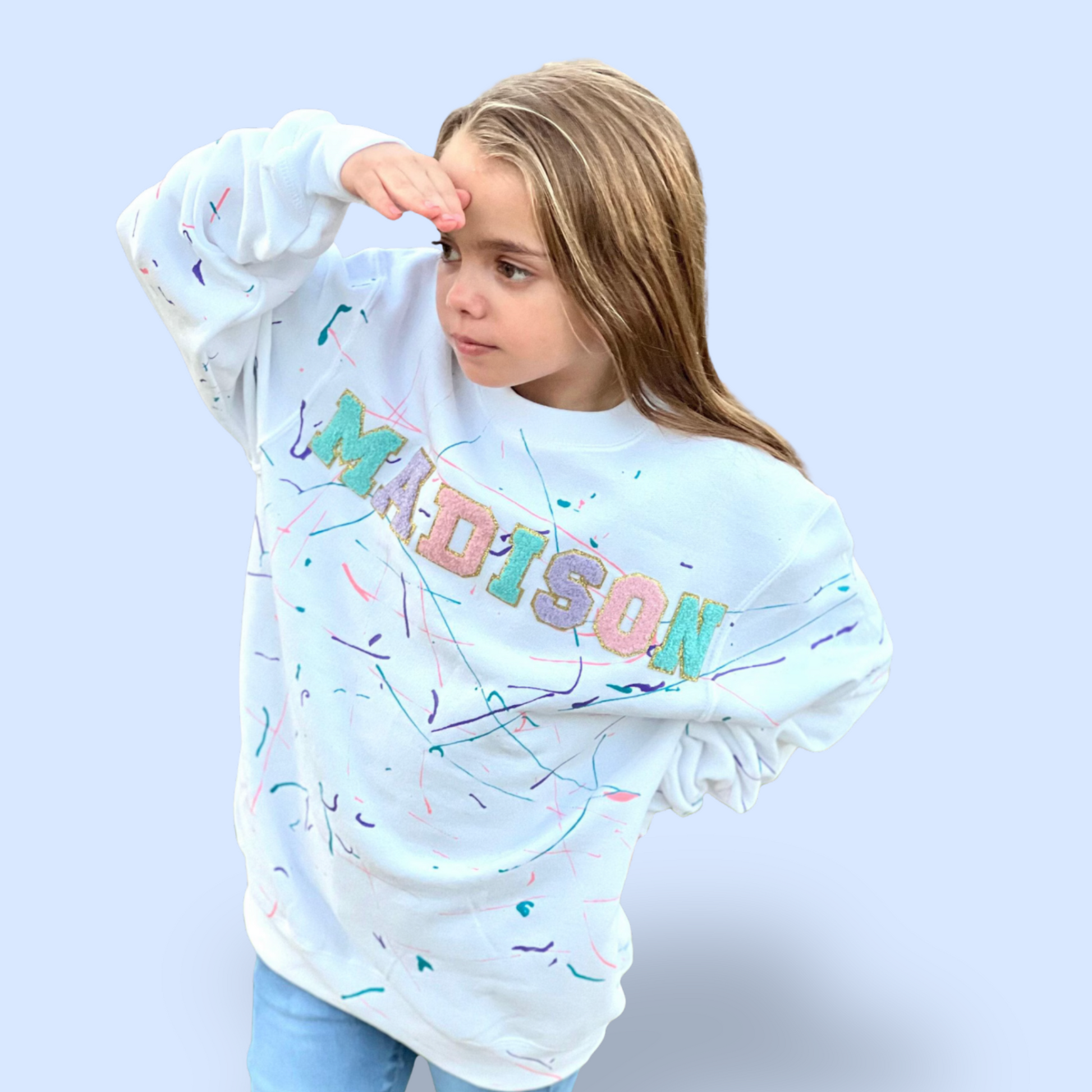 Child wearing a white sweatshirt with colorful text and patterns on a light blue background